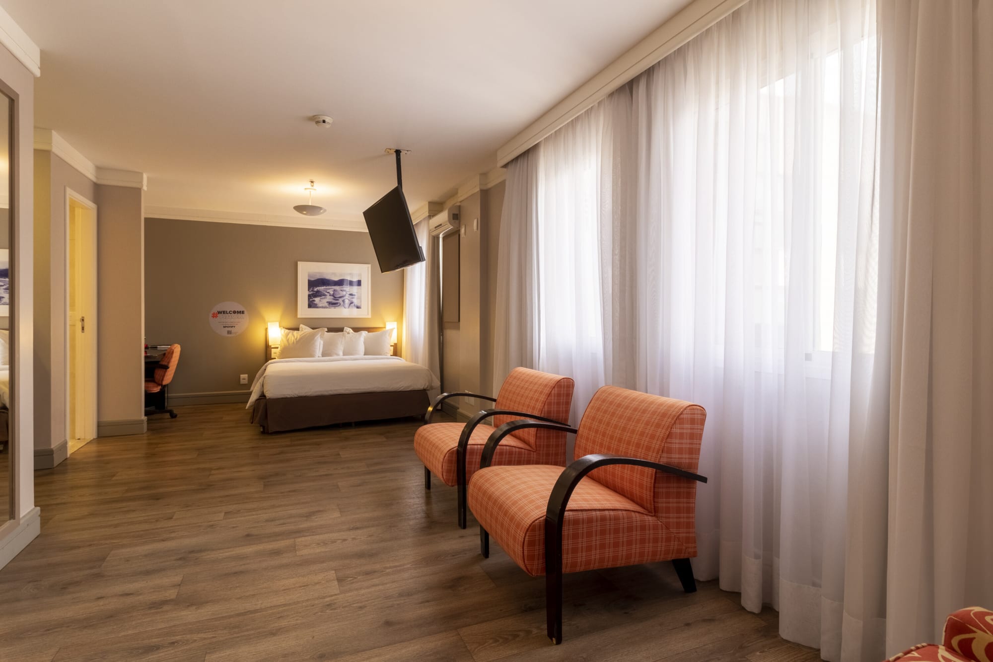 Long hotel room with two orange armchairs by sheer curtains