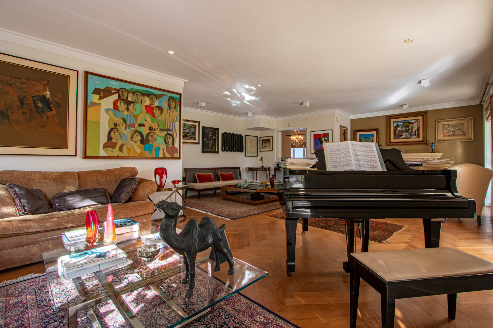 Sala comprida com sofá de couro, mesa de centro de vidro e piano de cauda sob os quadros