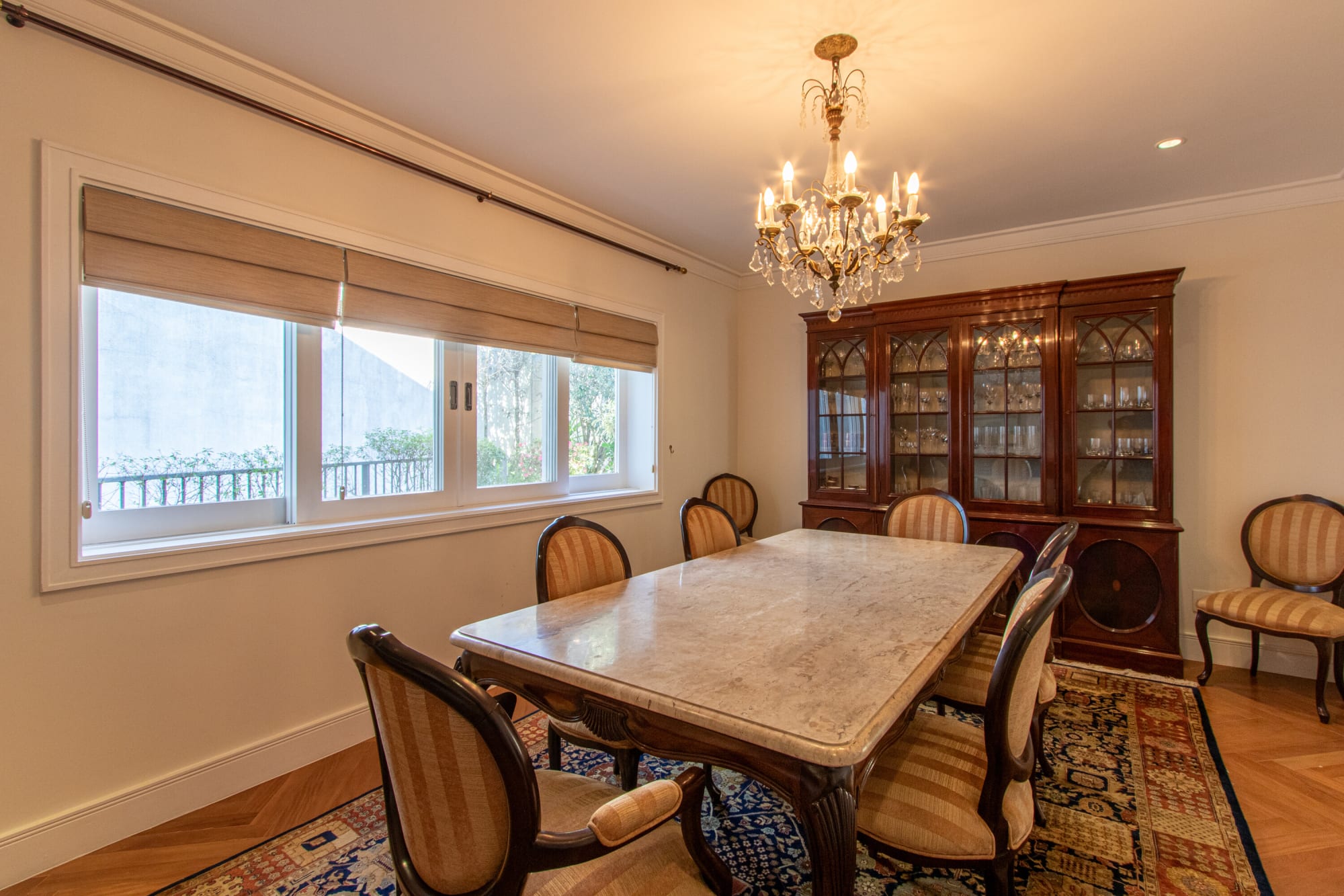 Sala de jantar com mesa de tampo de pedra, lustre de cristal e cristaleira com portas de vidro