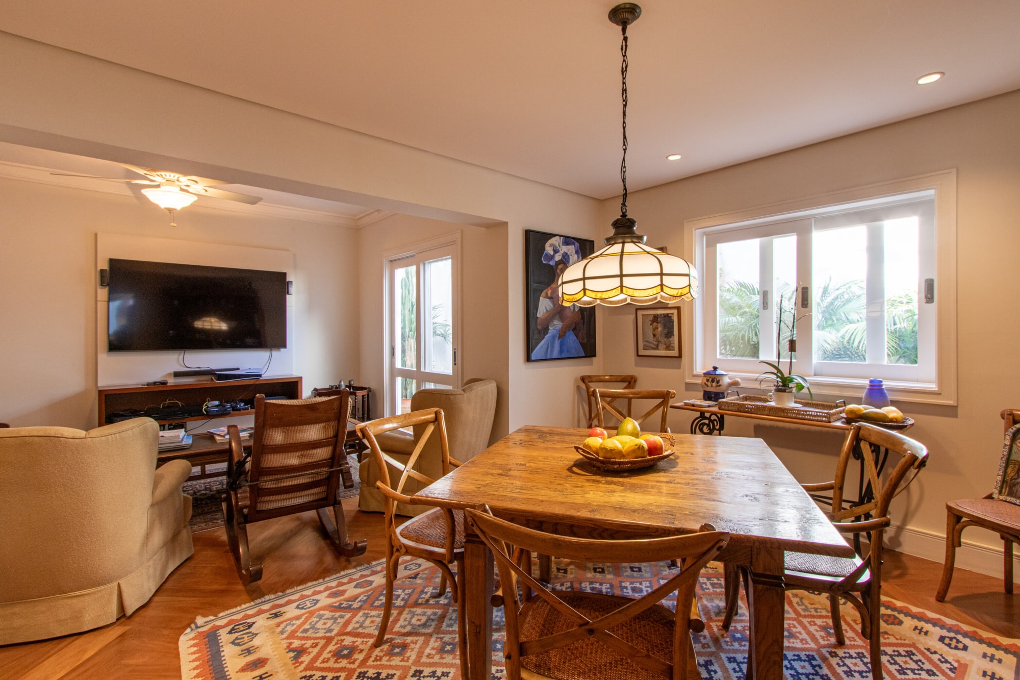 Sala íntima com mesa de fazenda, pendente estilo Tiffany, cadeira de balanço e televisão
