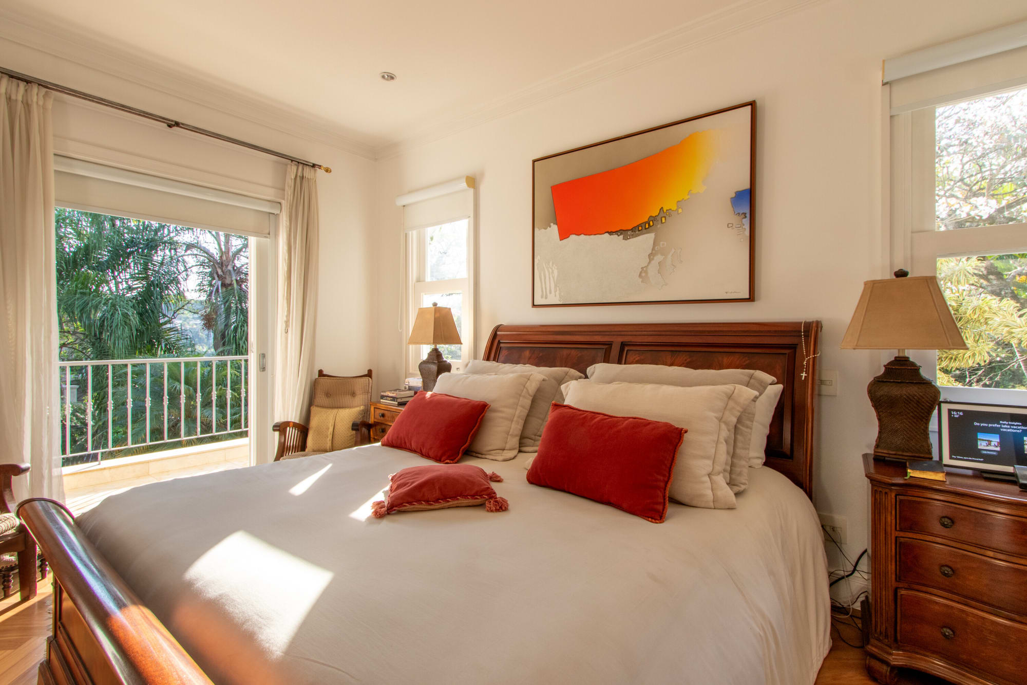 Quarto com cama de madeira entalhada, almofadas vermelhas e gravura abstrata laranja acima