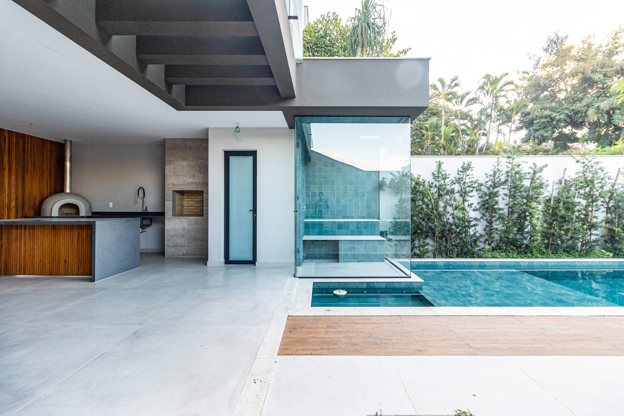 Empty covered terrace with pizza oven, glass shower box and pool edge