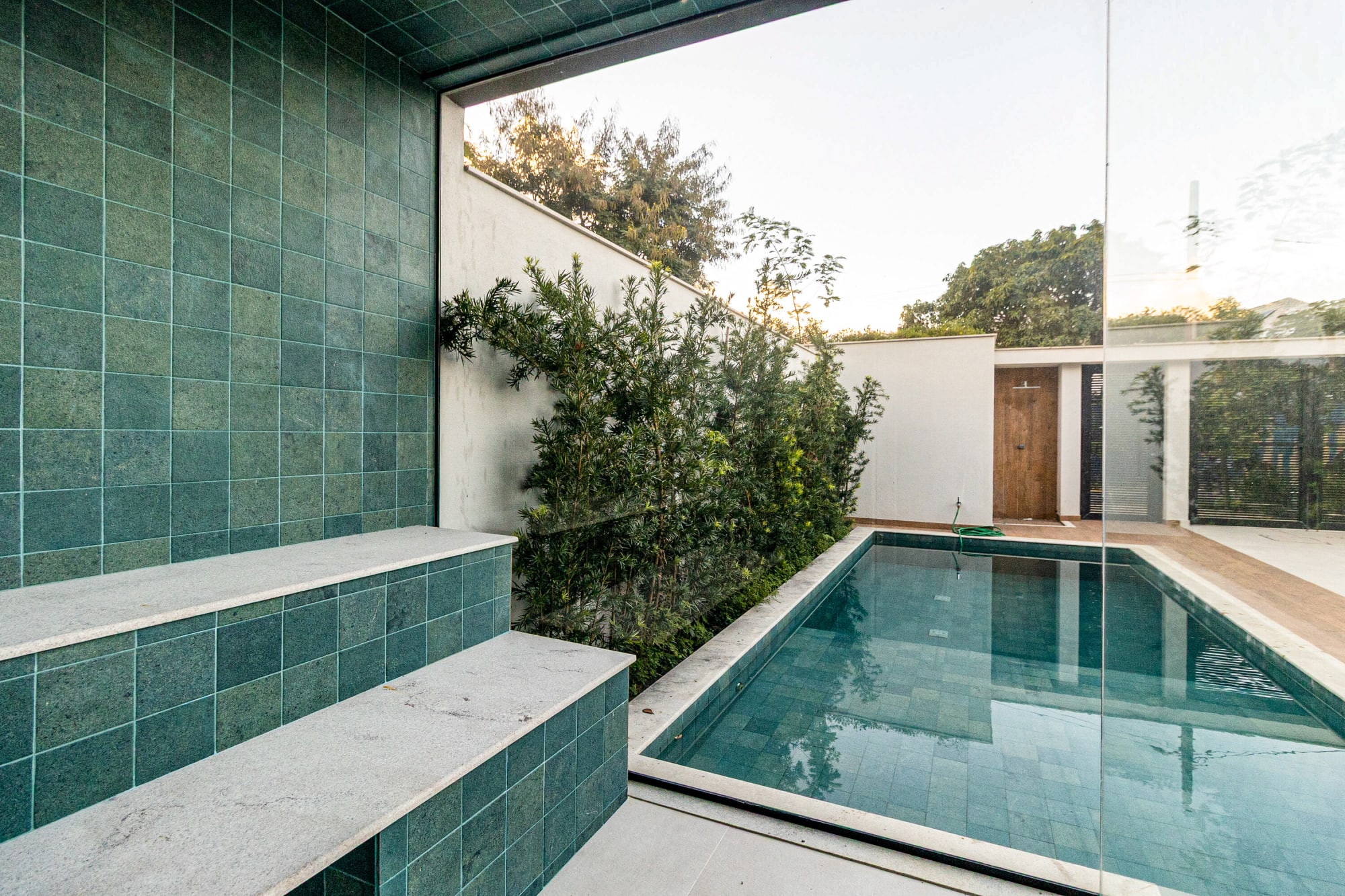 Green tiled pool wall and planted bed beside a narrow lap pool
