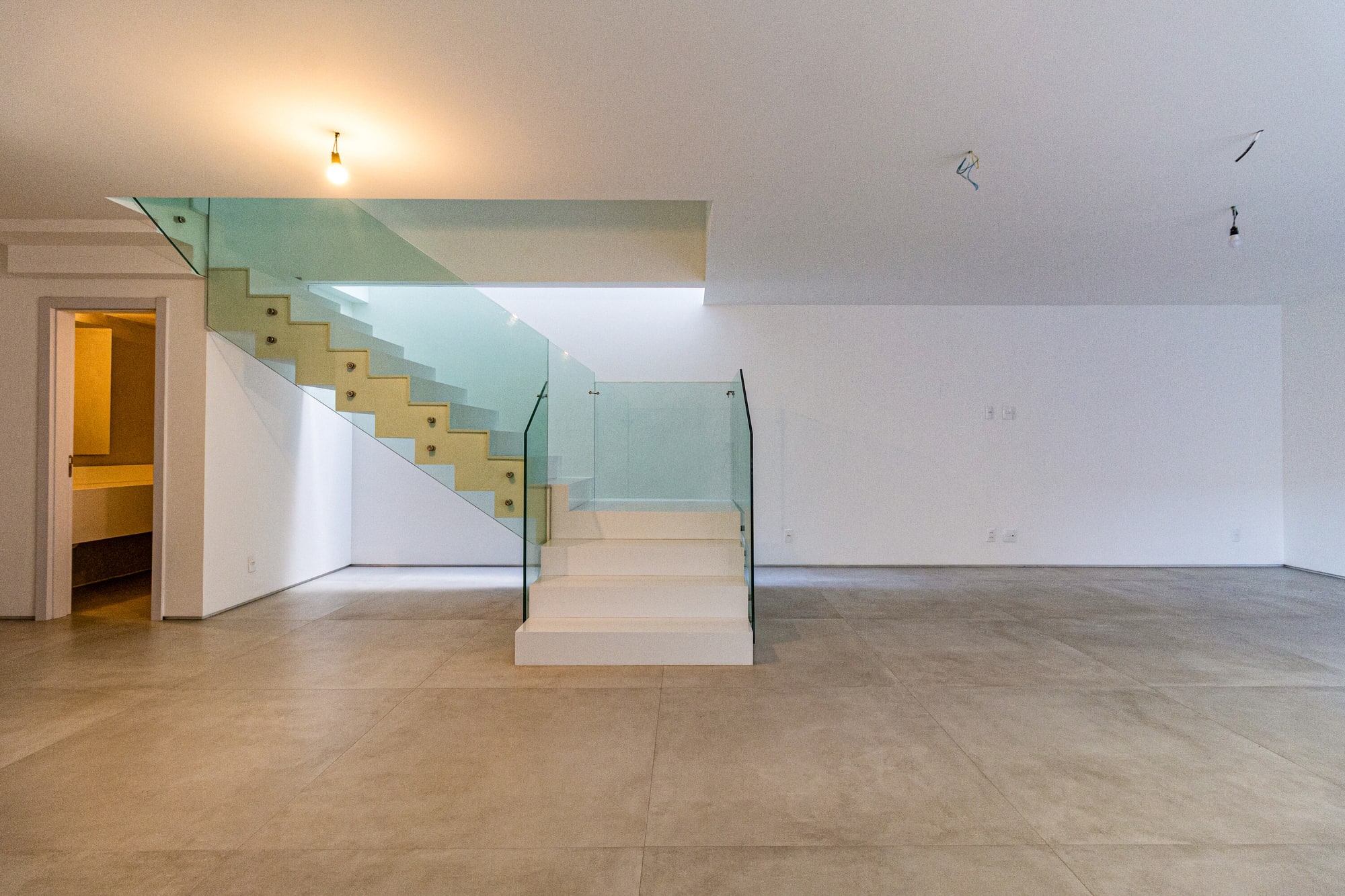 Empty living room with glass stair rising beside white walls