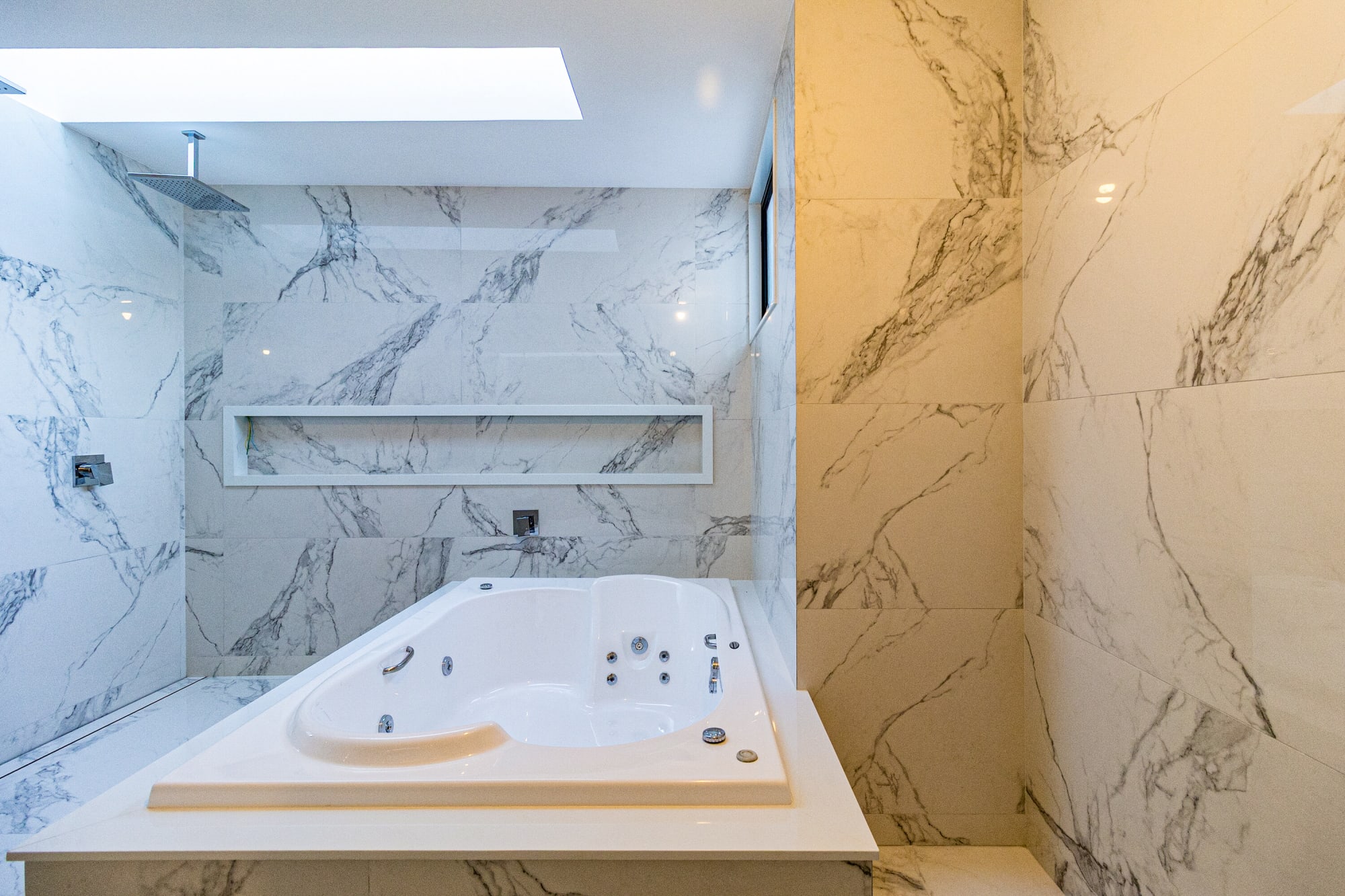 Marble clad bathroom with corner whirlpool tub and skylight
