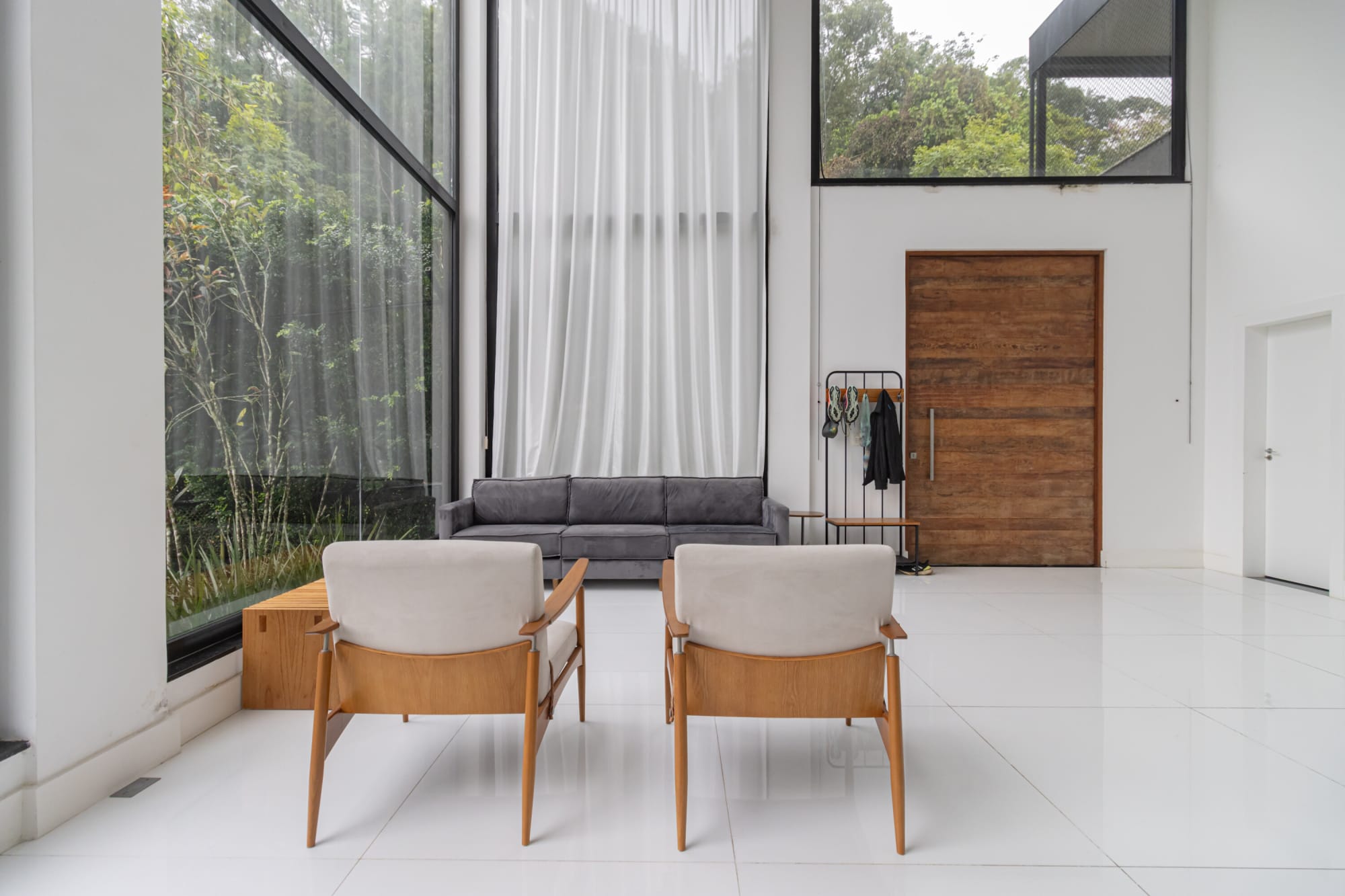 Two timber armchairs facing a glass wall and timber front door in a white hall