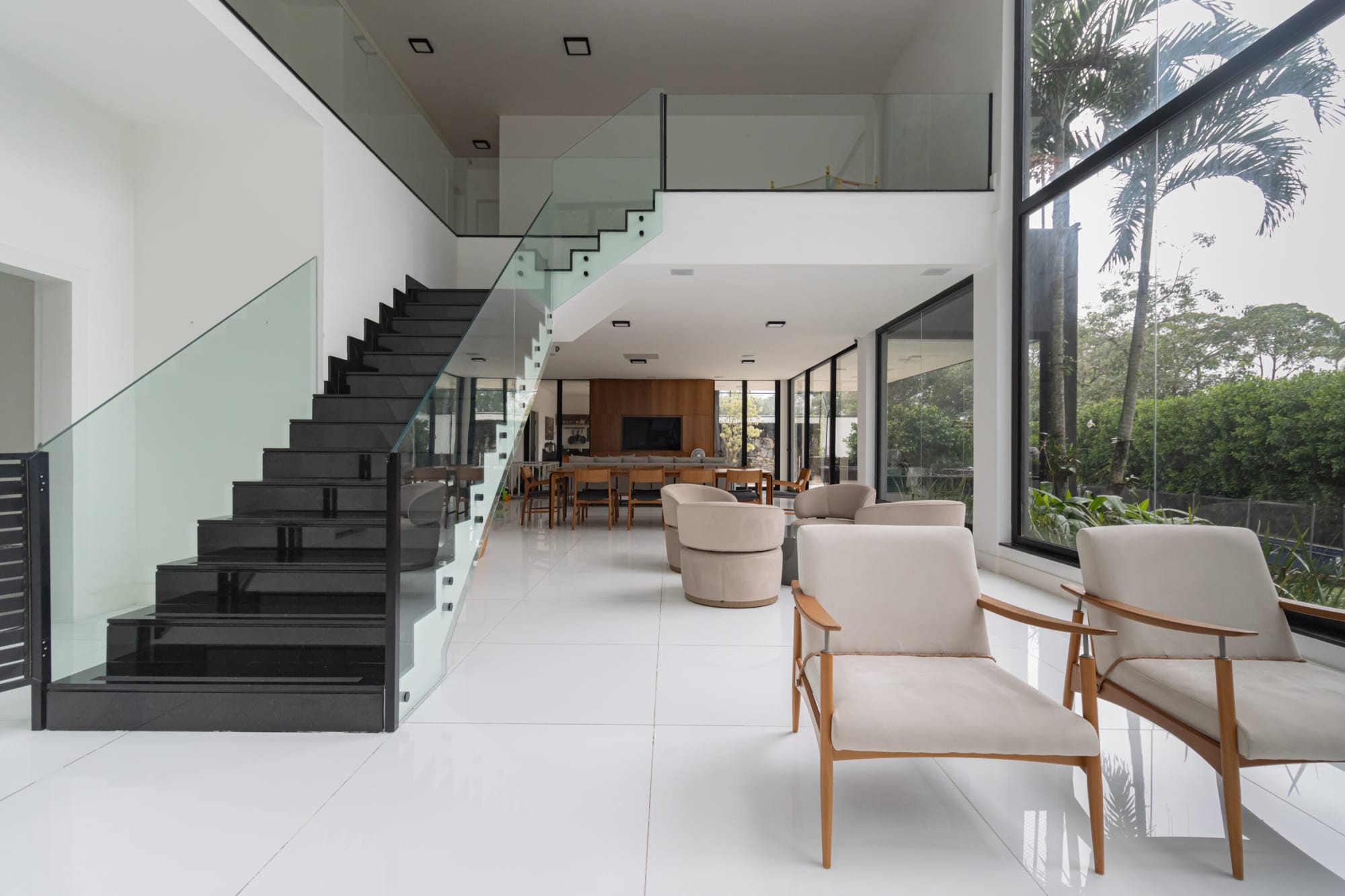 Black floating stair with glass rail rising over an open plan living room
