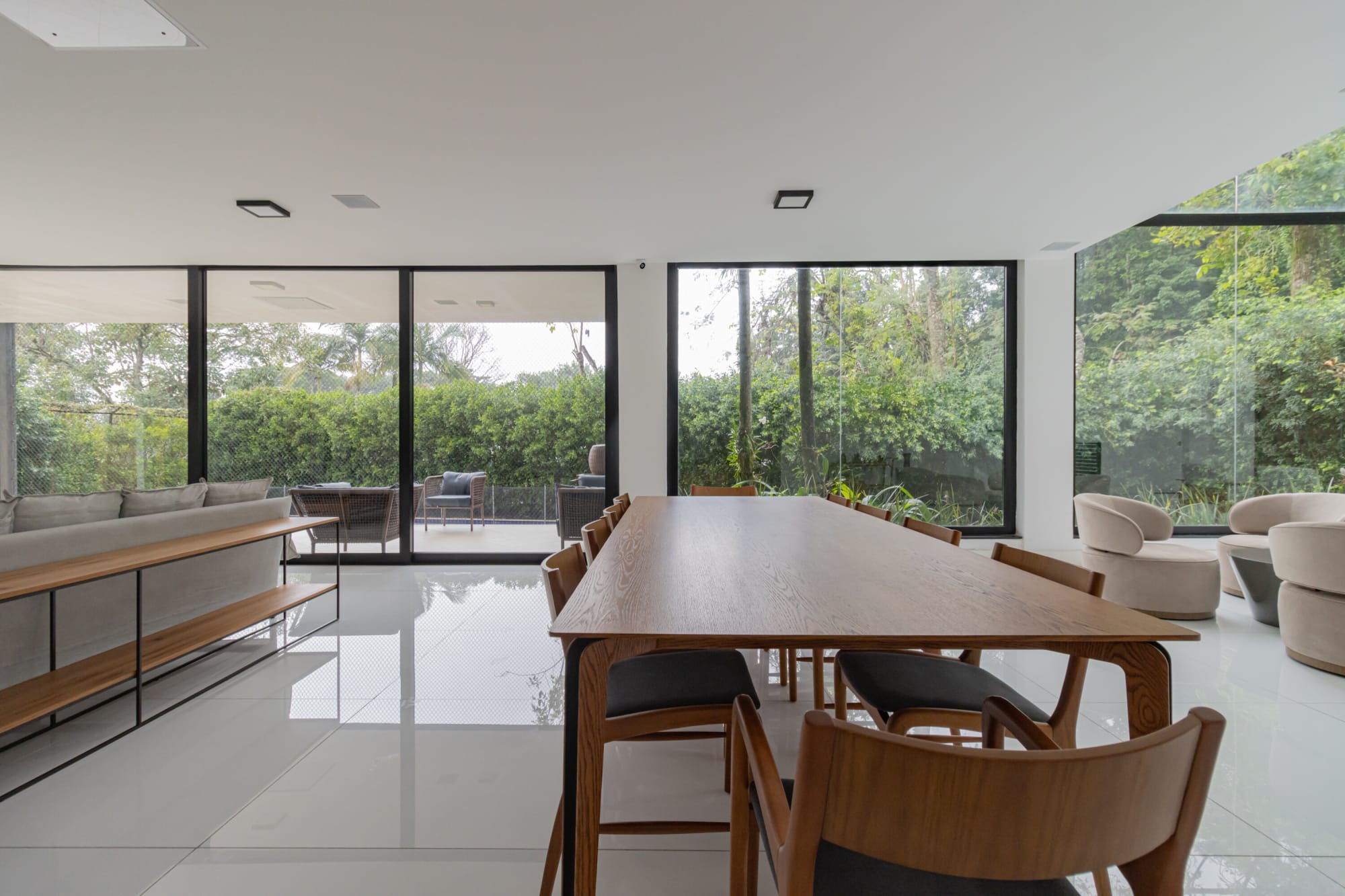 Long timber dining table on white tiles beside glass walls onto the garden