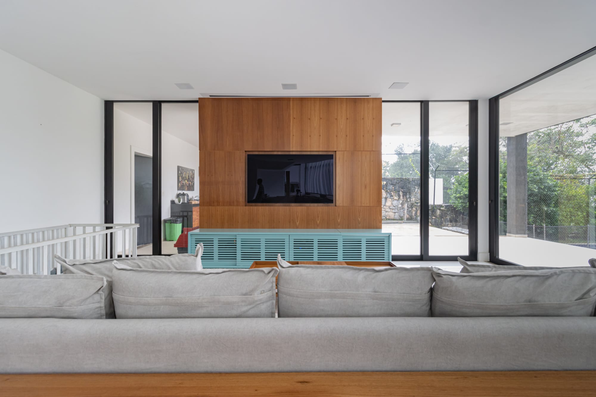 Long grey sofa before a timber panelled television wall and glass corners
