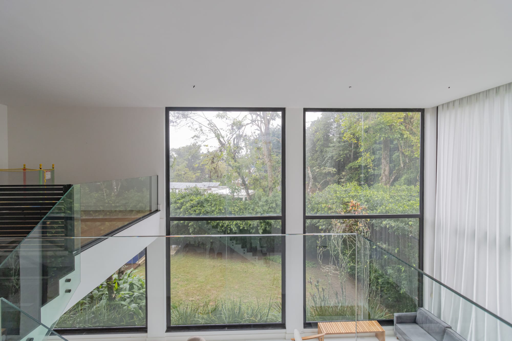 Glass gallery rail over the living room facing tall windows onto the trees