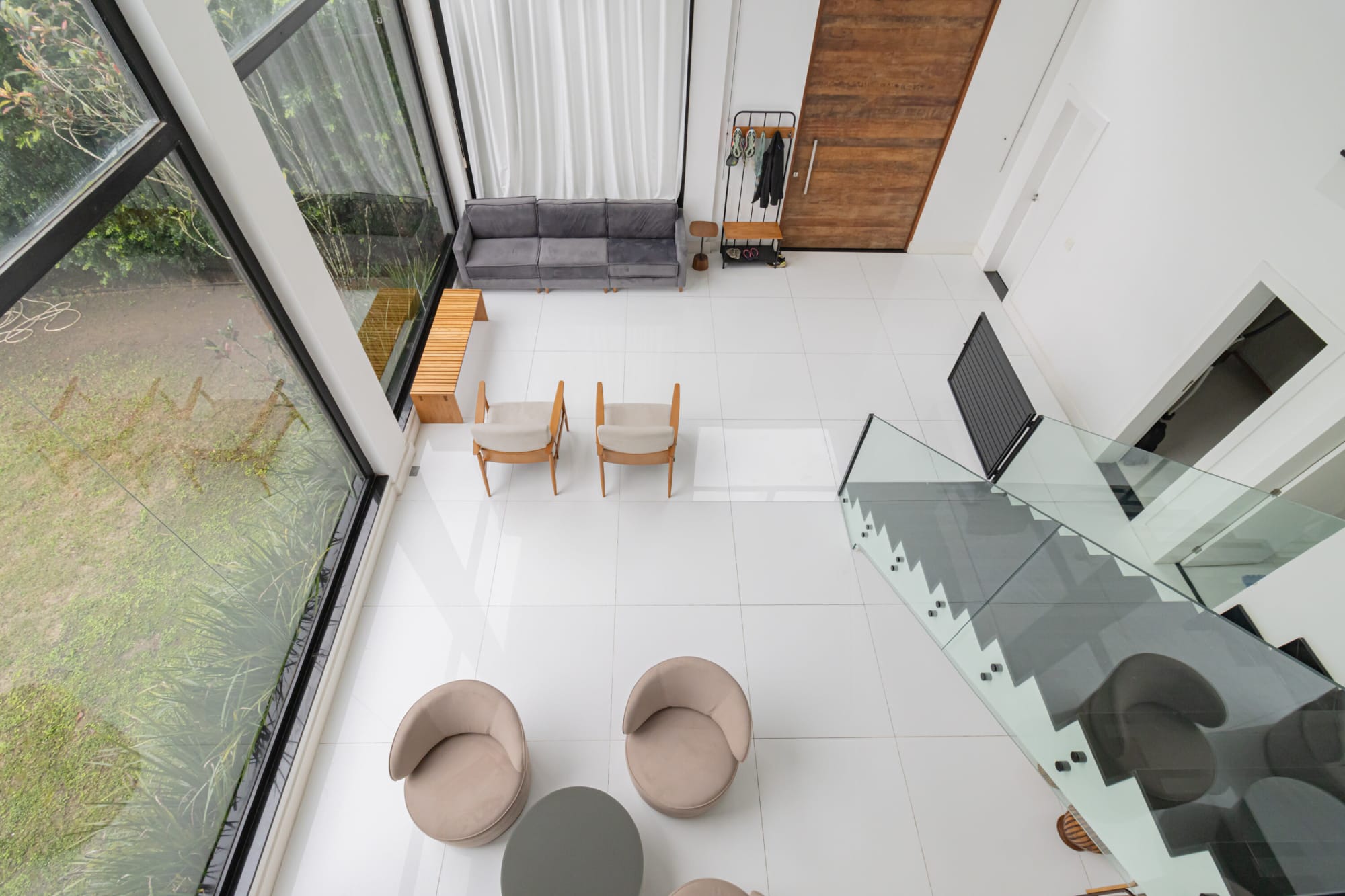 View down from the mezzanine onto armchairs, sofa and glass stair