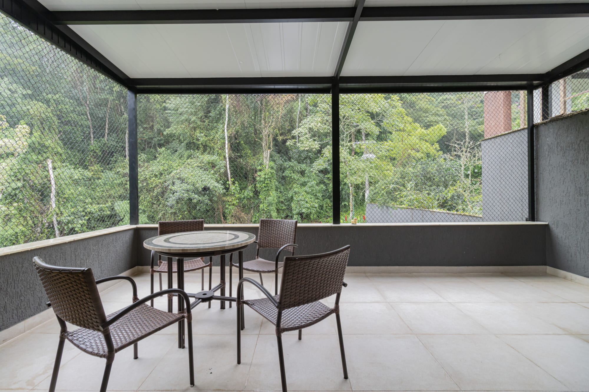 Screened terrace with rattan chairs and round table above the forest