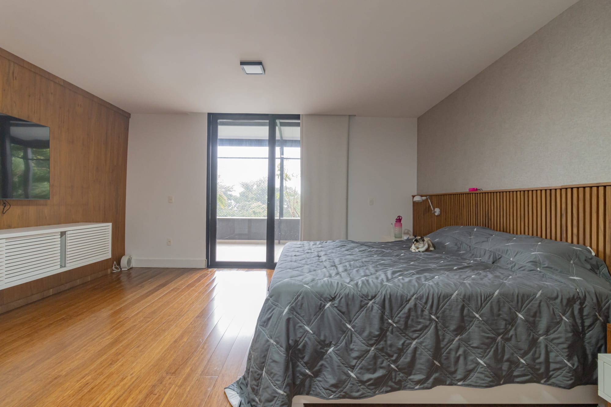 Bedroom with grey quilted bed, timber headboard and glass door to a balcony