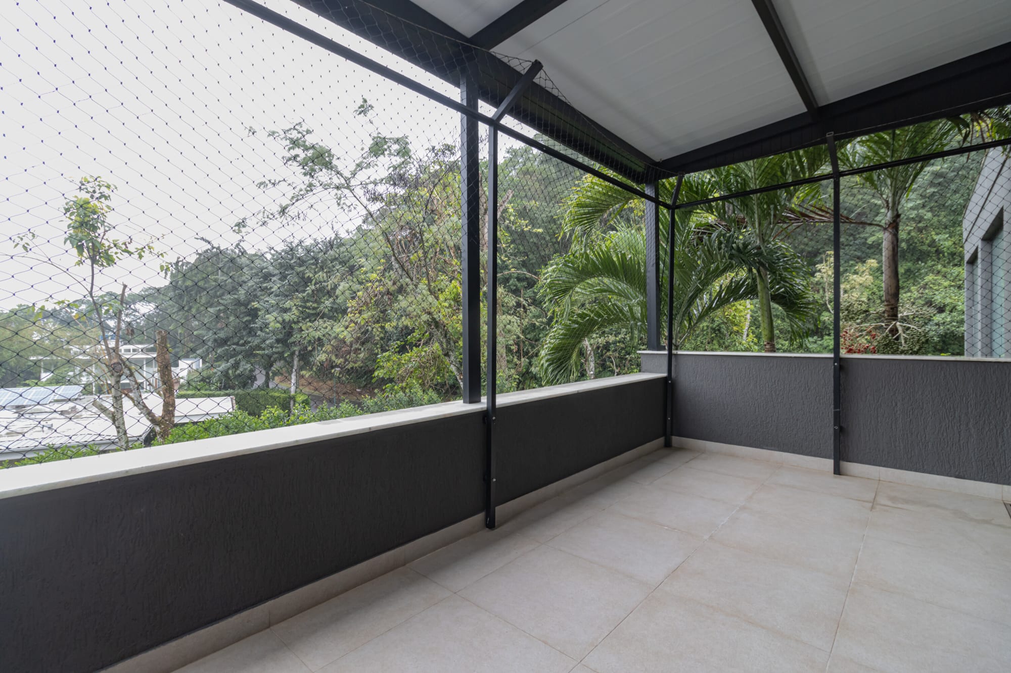 Empty screened terrace with dark parapet overlooking forest and palms