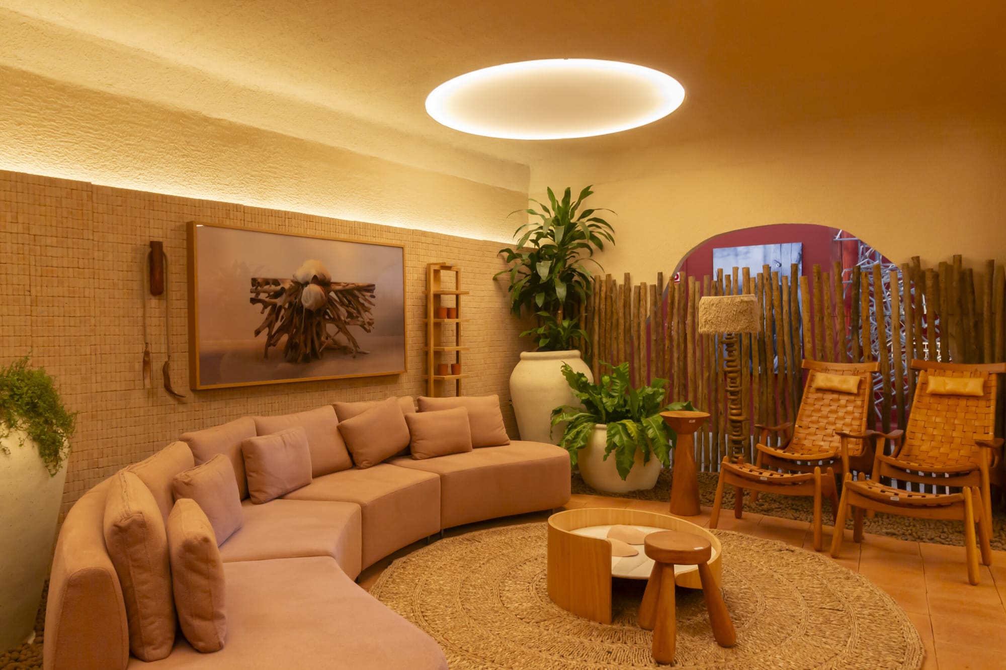 Blush sectional sofa, potted palm and timber lounge chairs beside a pole screen in warm cove light