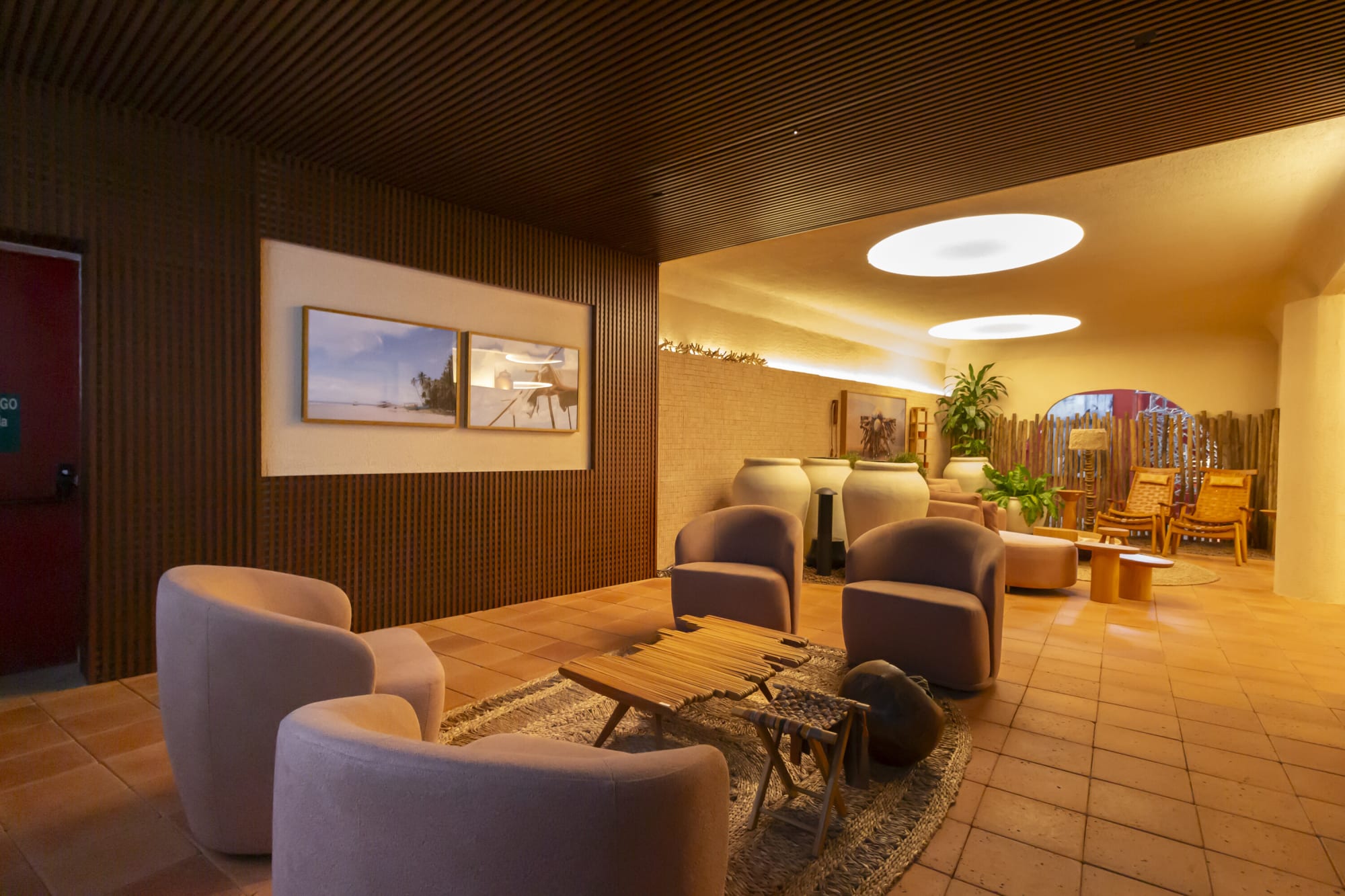 Lilac armchairs around a low timber table on terracotta tile under a dark slatted wall