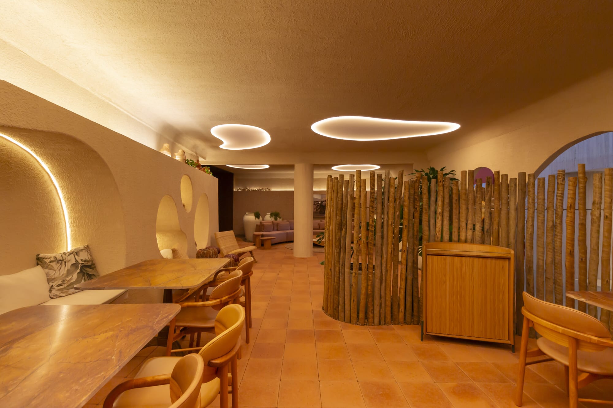 Banquette dining tables beside a round pole screen enclosure under organic ceiling light coves