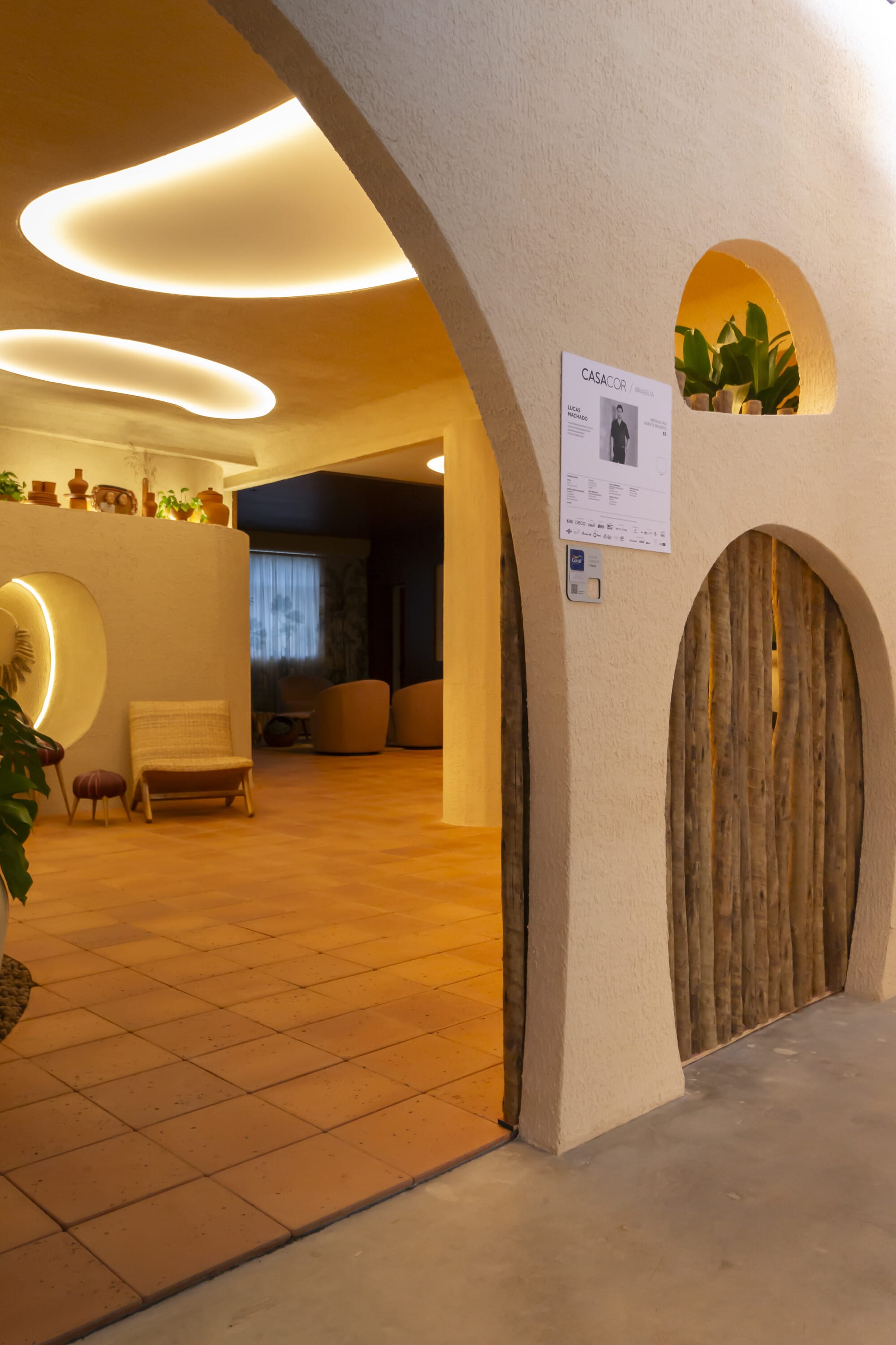 Tall plaster arch opening onto a terracotta corridor with a pole screen door and lit niches