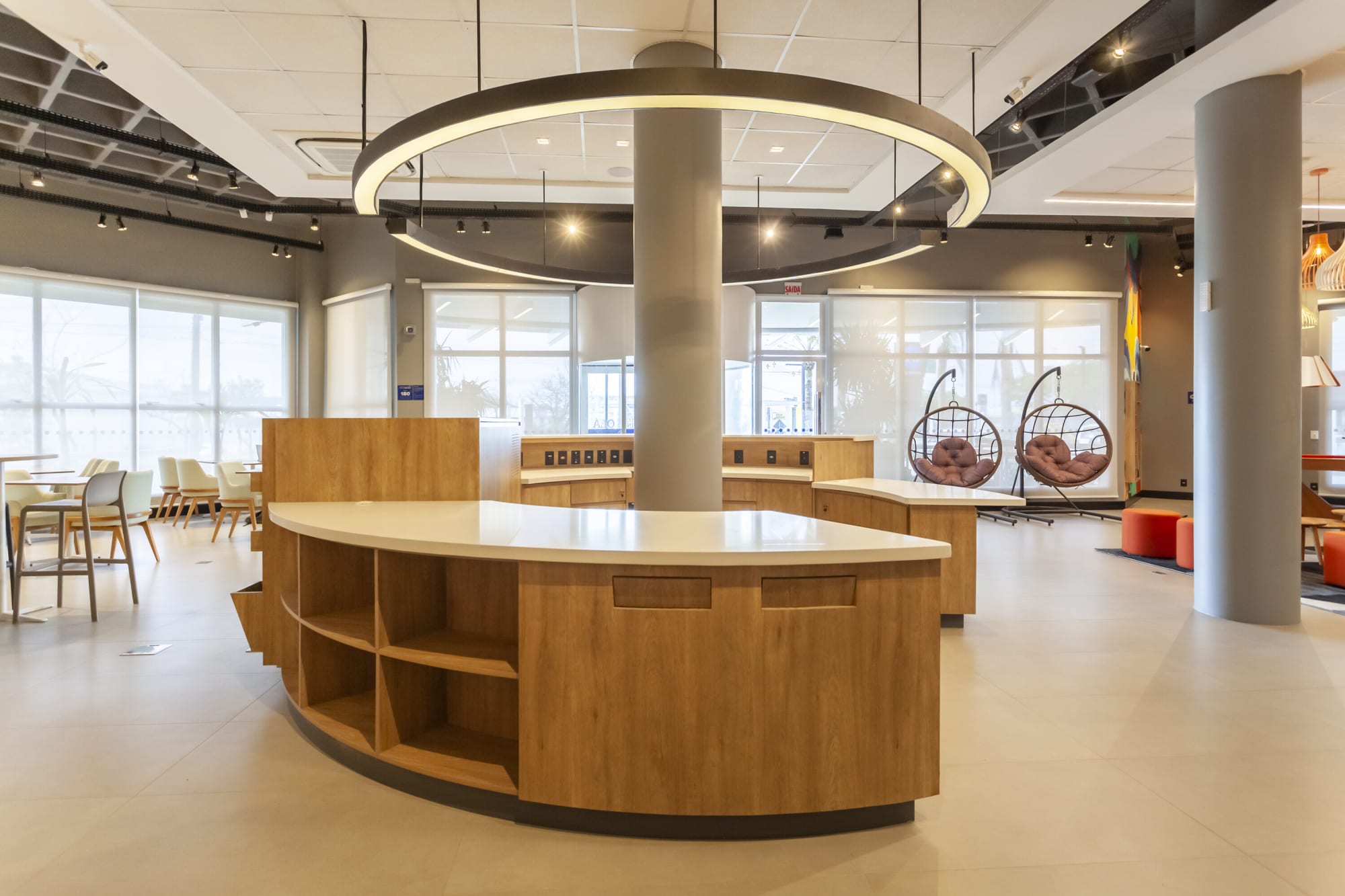 Open lobby with curved timber counter, ring light and hanging rattan chairs