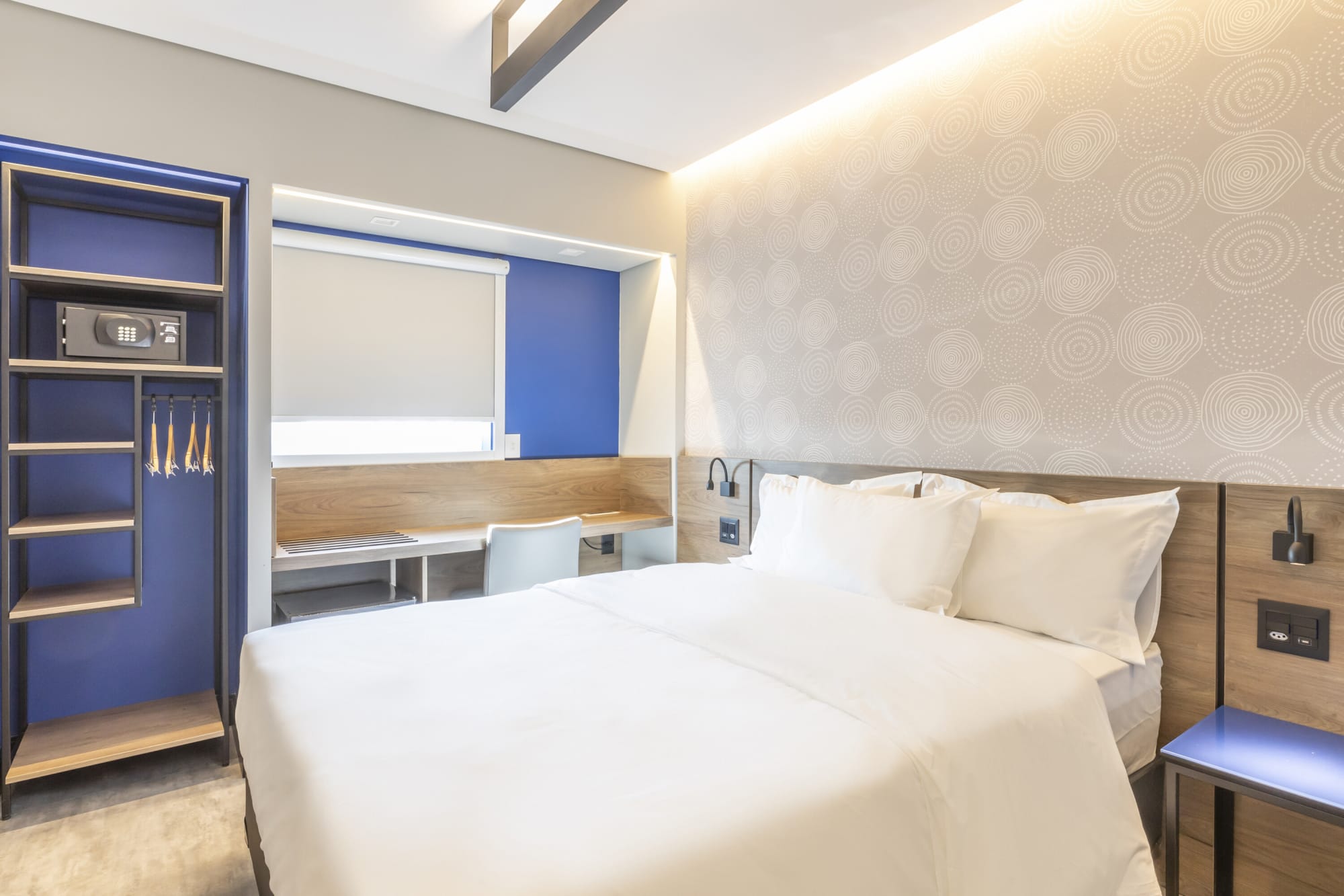 Hotel room with white bed, cobalt blue wardrobe and window desk