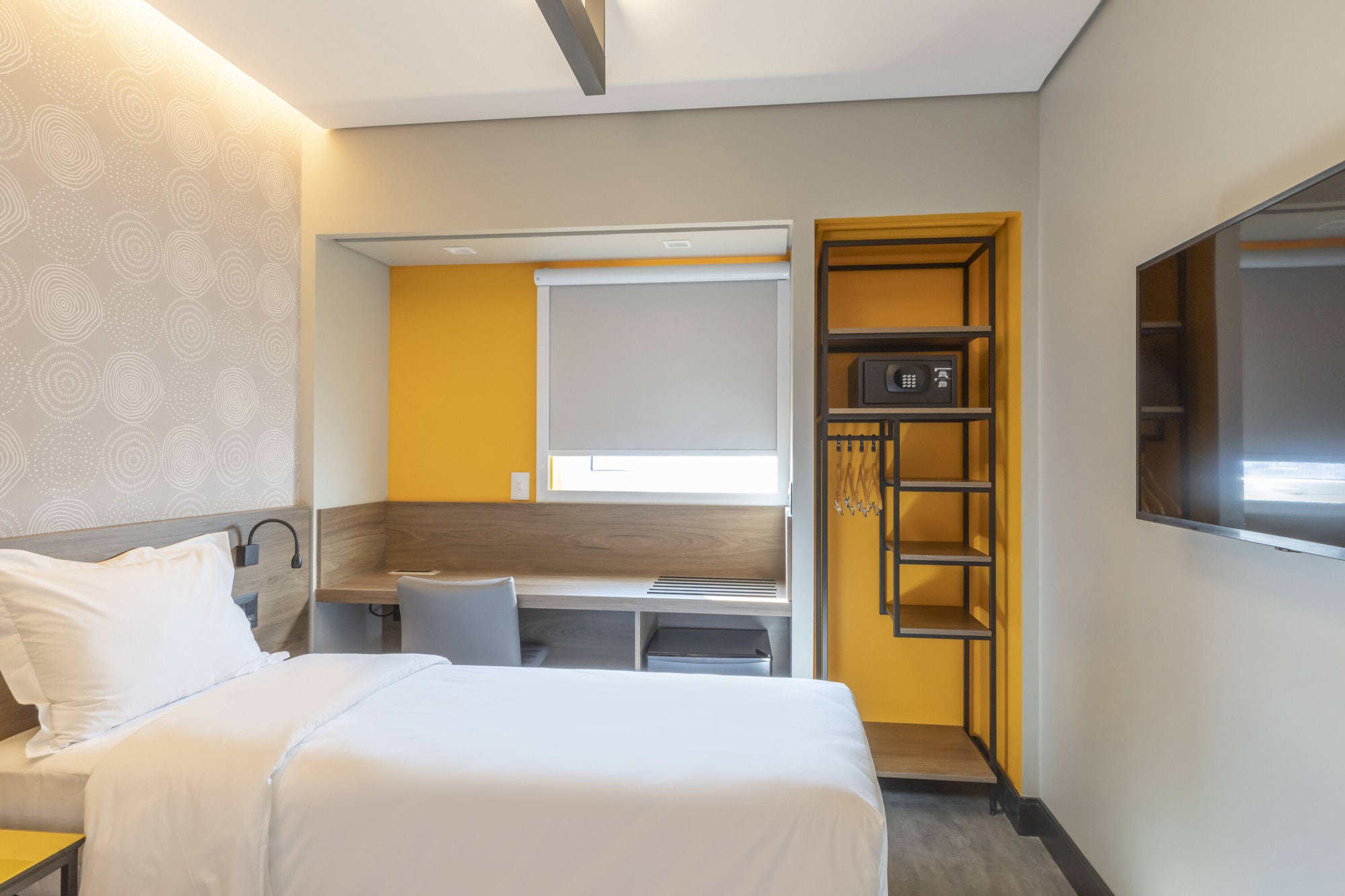 Hotel room with white bed, mustard yellow wardrobe and grey patterned wall