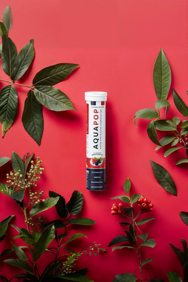 Aquapop tube centred among dark green leaves and berry sprigs on berry red