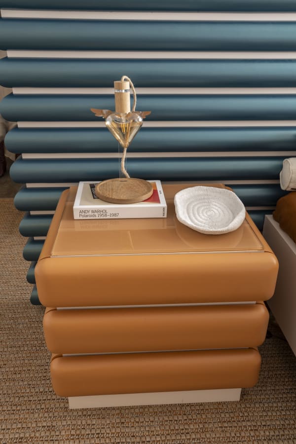 Stacked tan leather bedside chest with a sculpture and books against teal bolsters