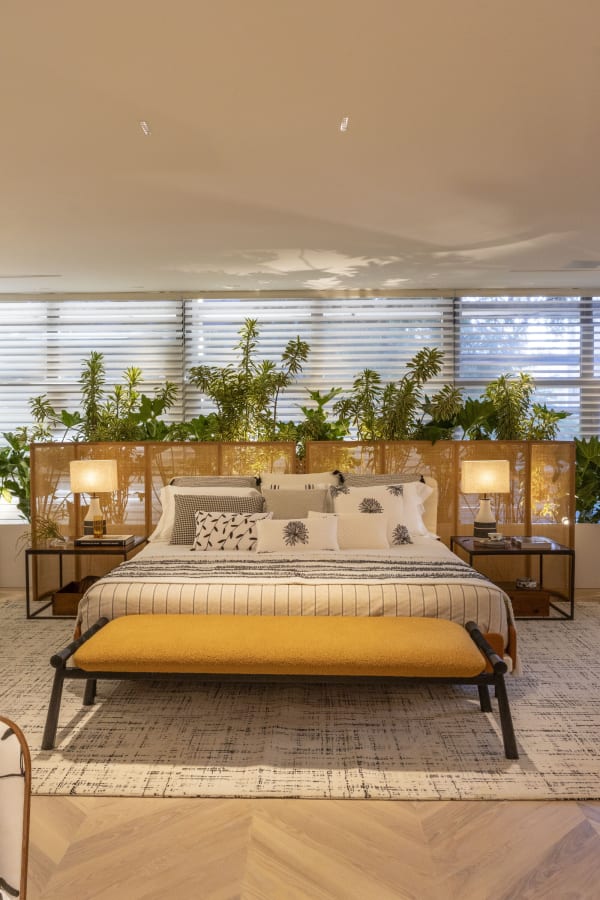 Master suite at CASACOR São Paulo with a cane headboard, plants and mustard bench