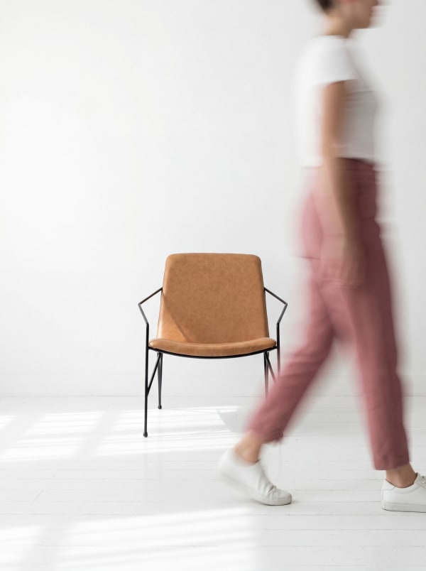A model in pink trousers walking past a tan leather Cremme chair on a black frame