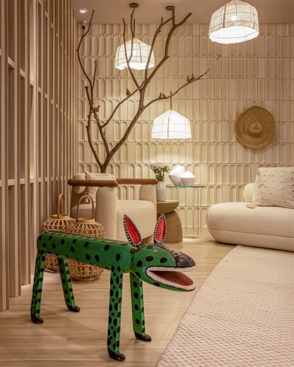 Green spotted folk-art jaguar before a cream bouclé sofa, timber slat screen and paper lanterns on a bare branch