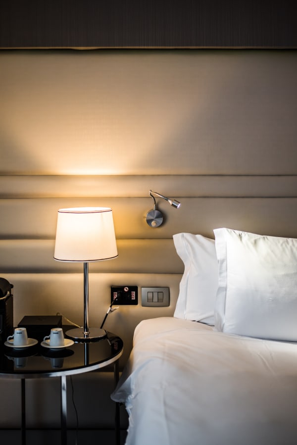 Bedside table with lamp and cups beside crisp white pillows in warm light