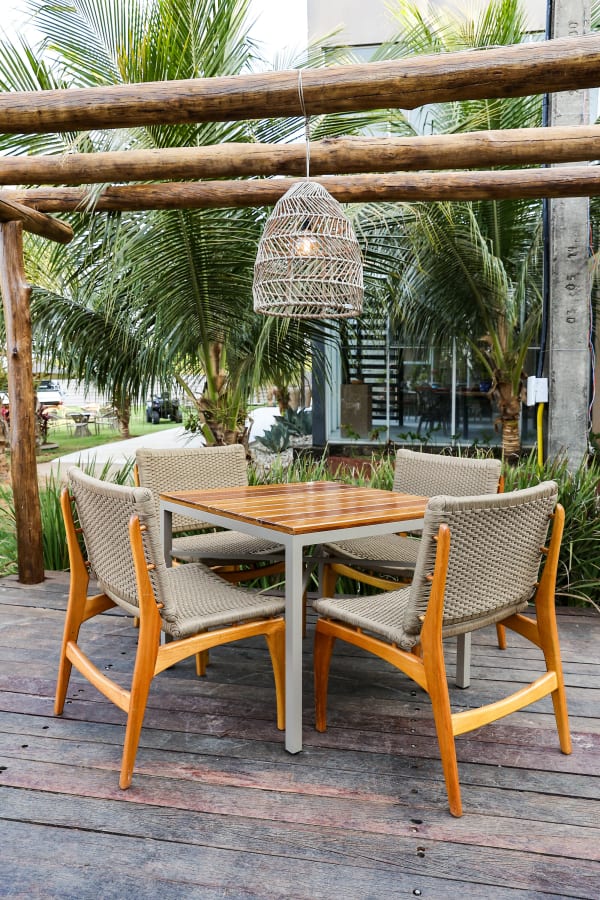Teak dining table with rope chairs under a woven pendant and log beams