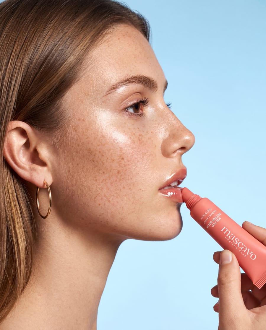 Mascavo lip tube touched to the lips in profile against a pale blue sky