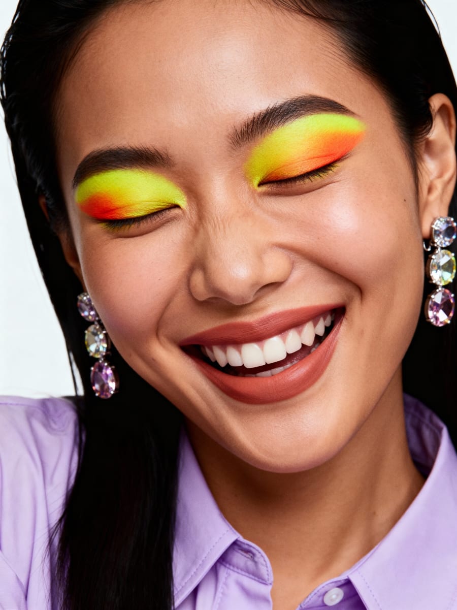 Neon yellow to orange eyeshadow with crystal drop earrings and a lilac shirt