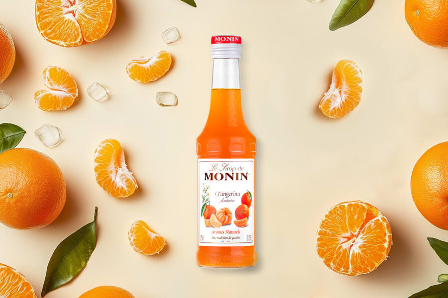 Monin tangerine syrup bottle with peeled tangerine segments and ice on a cream surface