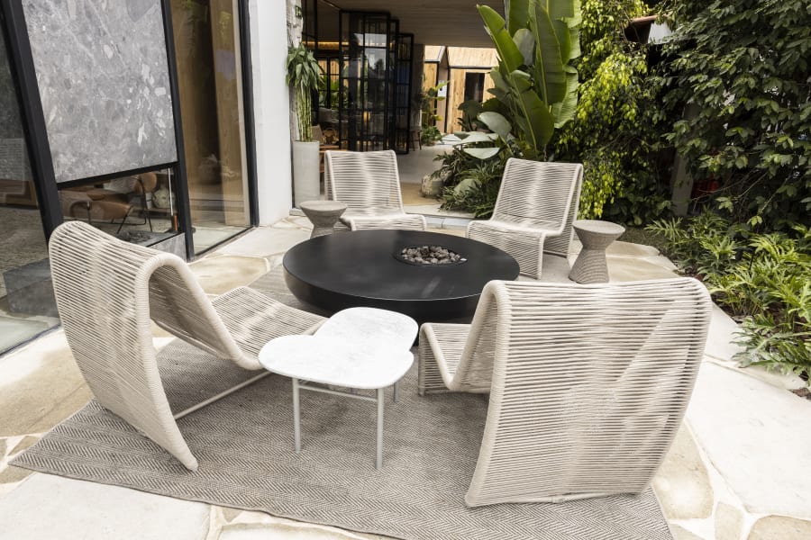 White rope lounge chairs around a black round table on a garden patio