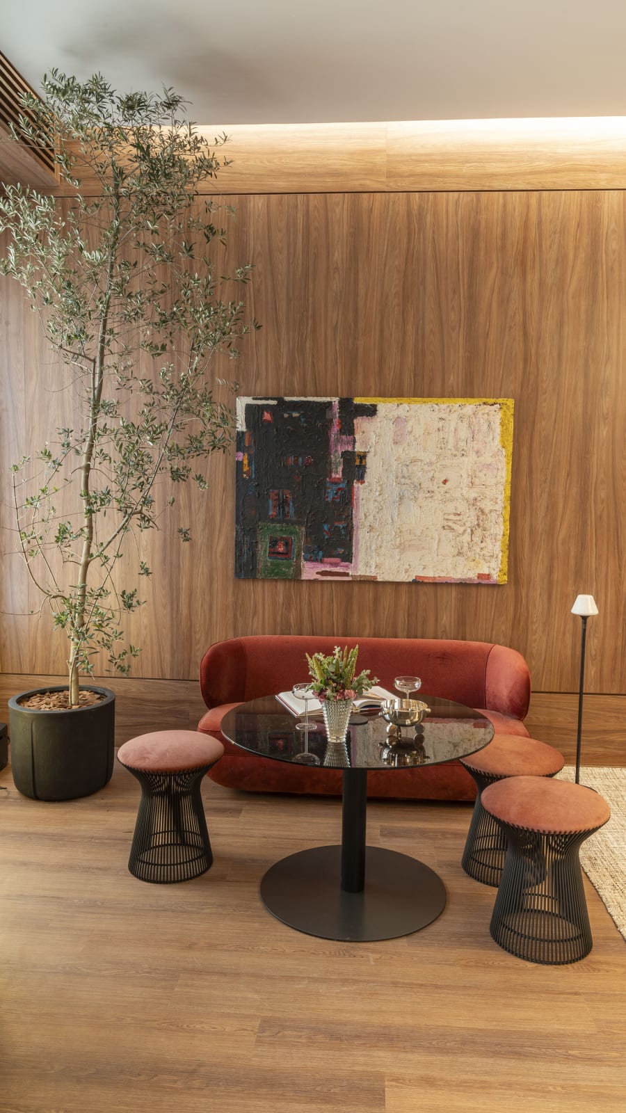 Red velvet banquette, round table and woven stools beside an olive tree in a walnut room