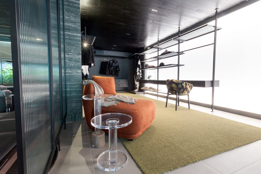 Orange chaise and acrylic side table on a green rug beside fluted glass panels
