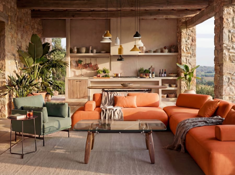 An orange modular Cremme sofa and glass coffee table in a stone walled kitchen living room