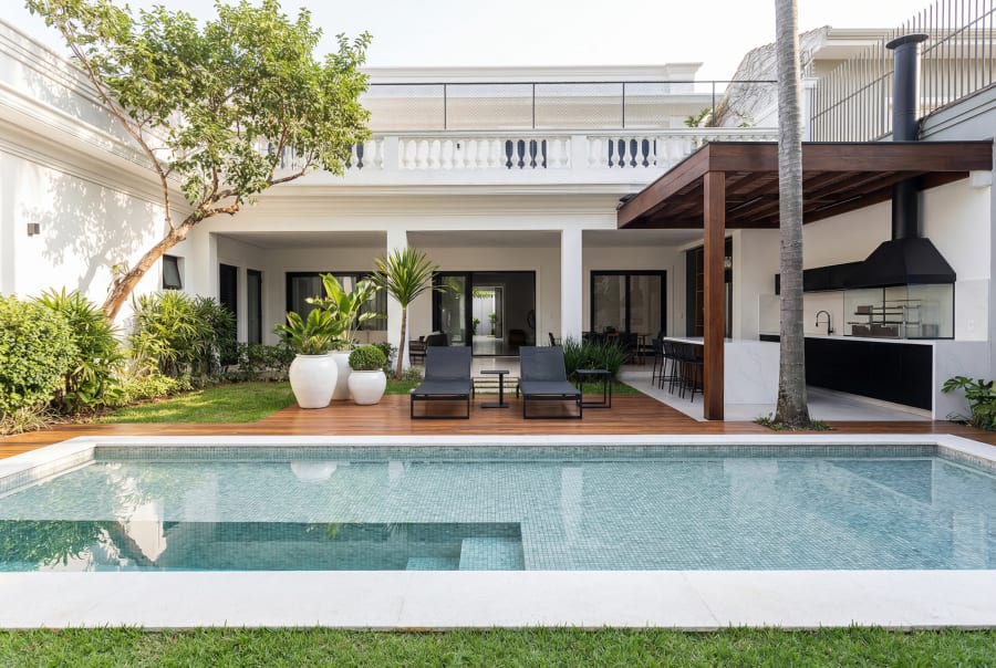 White house with pool, lawn and covered barbecue terrace staged with loungers