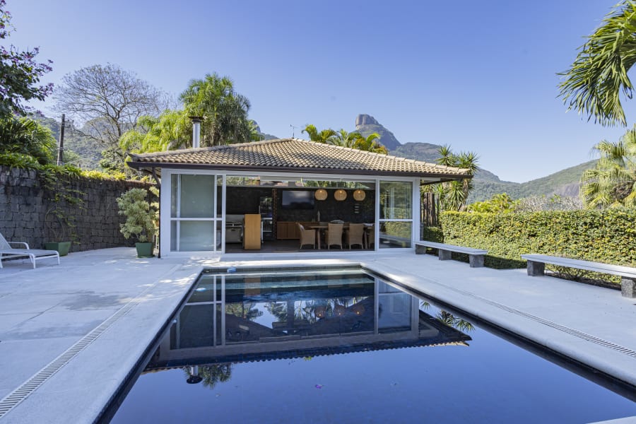Rectangular pool before a tiled roof pool pavilion with Pedra da Gávea in the distance