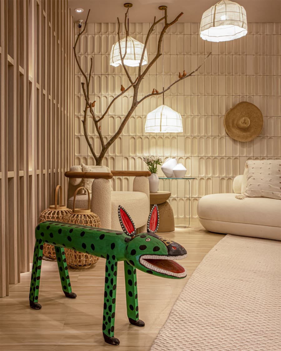 Green spotted folk-art jaguar before a cream bouclé sofa, timber slat screen and paper lanterns on a bare branch