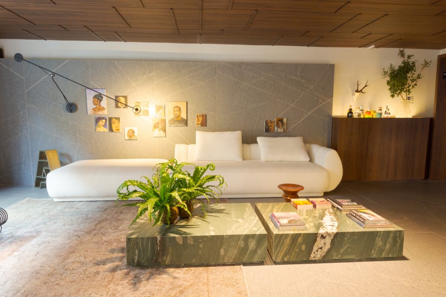 White curved sofa and green marble coffee table under a walnut panelled ceiling with framed sketches