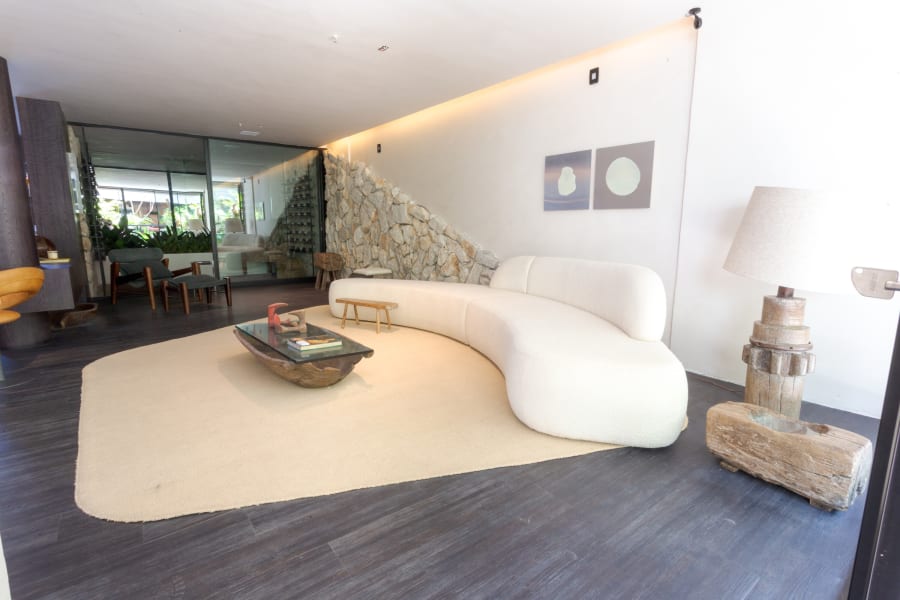 Curved white sofa on a cream rug beside a diagonal stone wall and a garden view