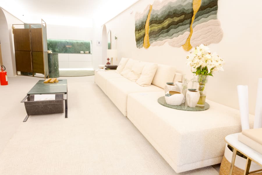 Long white sofa beneath a wavy green and gold wall hanging in a pale lounge