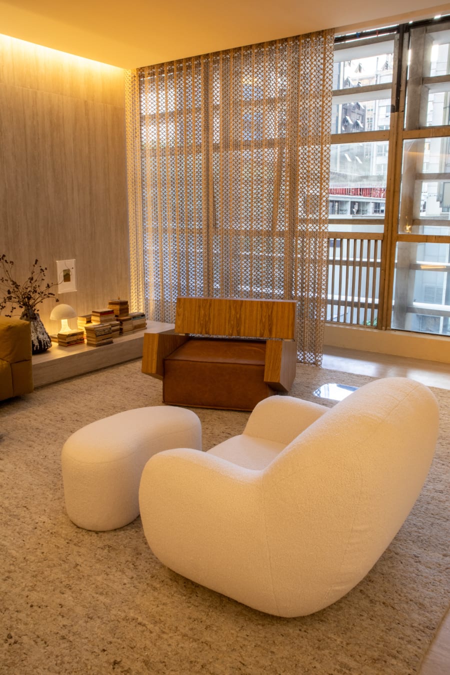 Cream boucle armchair and pouf on a pale rug before a perforated metal screen and windows