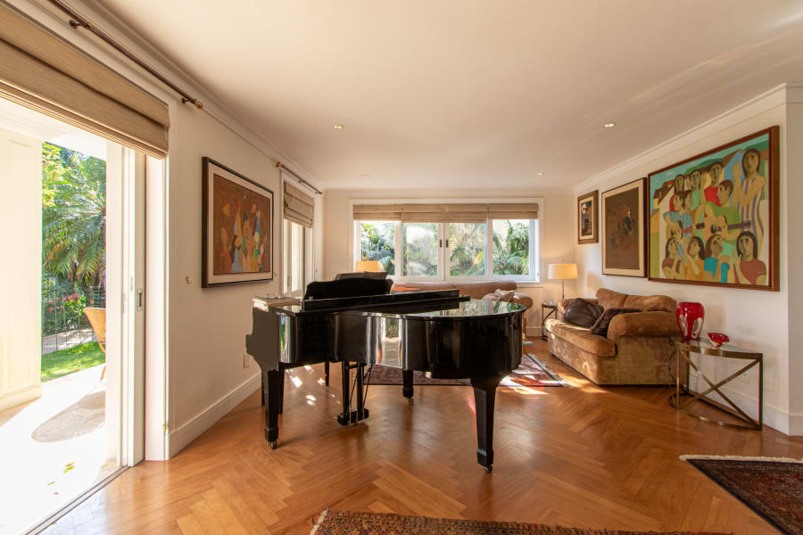 Living room with black grand piano, herringbone oak floor and paintings on cream walls