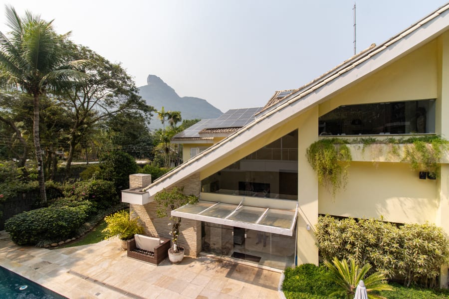 Cream house with steep sloped roof and glass awning, Pedra da Gávea behind
