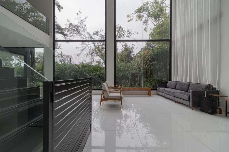 Double height glass living room with grey sofa, sheer curtains and forest view