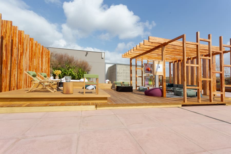 Rooftop timber deck with slatted pergola, lounge seating and a purple pouf under a blue sky